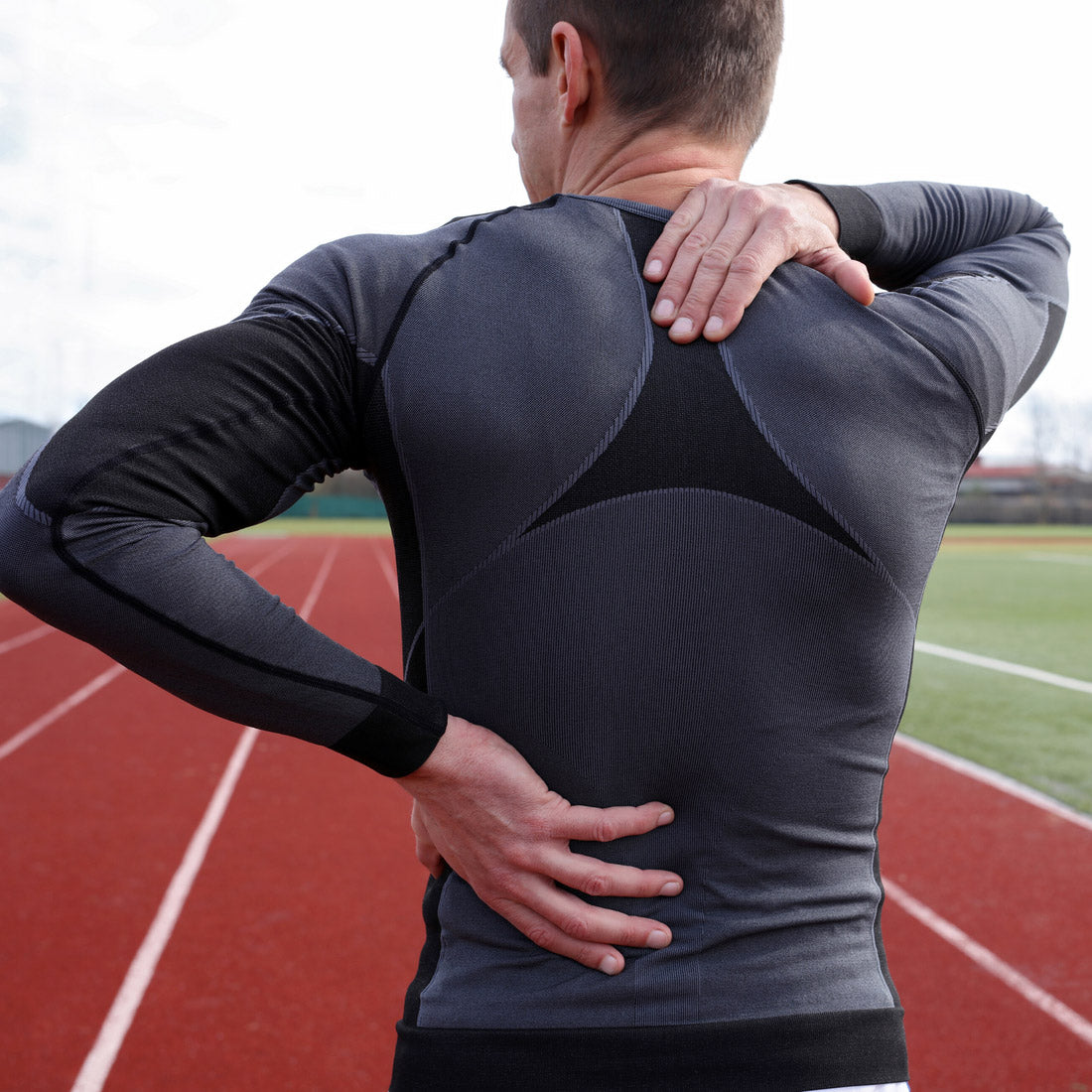 Runner holding his lower back in pain on an outdoor red running track