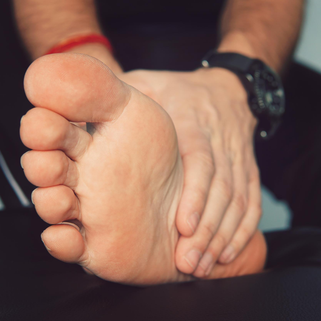 Person holding their bare foot with both hands, sole facing camera to indicate foot pain or discomfort