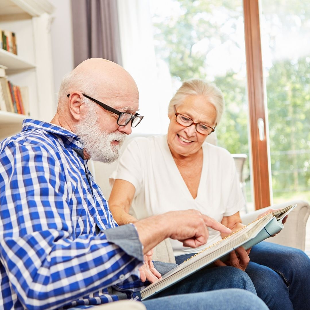 Elderly couple sitting in a sunlit living room looking through a photo album together