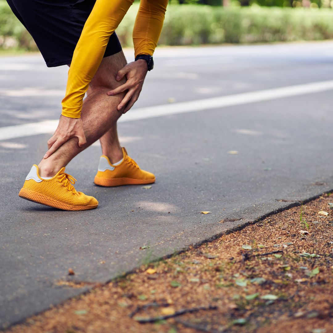 Runner stretching and holding the back of their lower leg near the Achilles tendon on a paved path