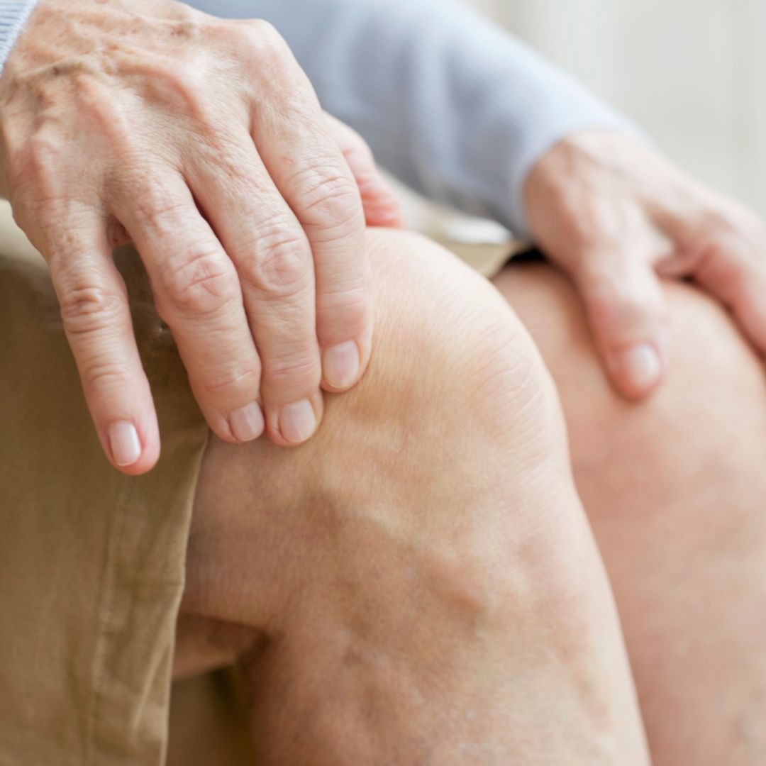Close up of an older person resting their hands on a knee suggesting joint pain
