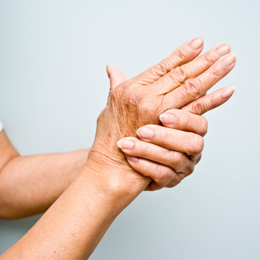 Older hands clasping the wrist, showing joint pain and stiffness against a pale background