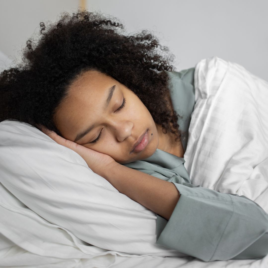 Woman with curly hair sleeping on her side in bed under a white duvet
