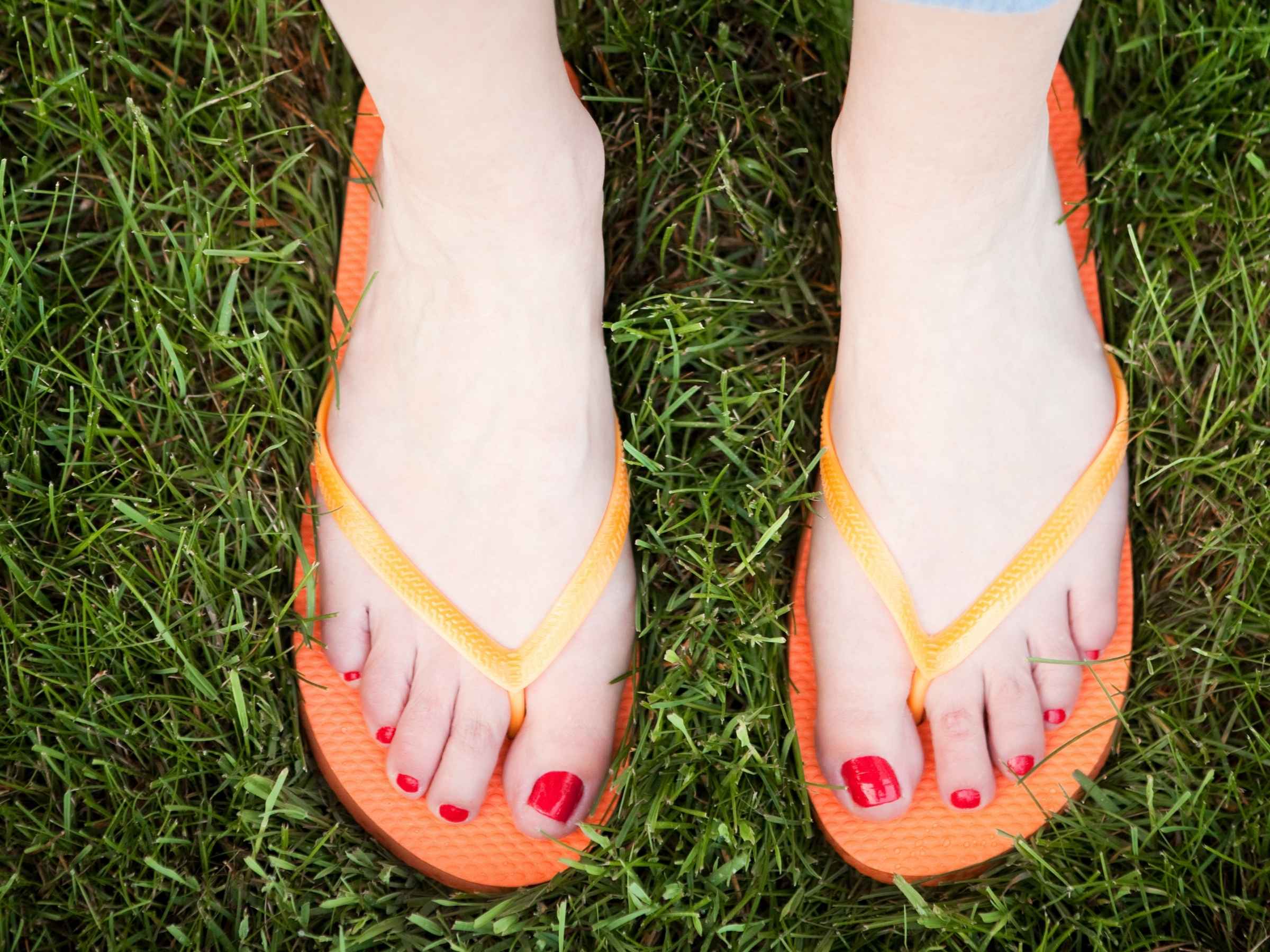 Feet wearing orange flip-flops standing on grass