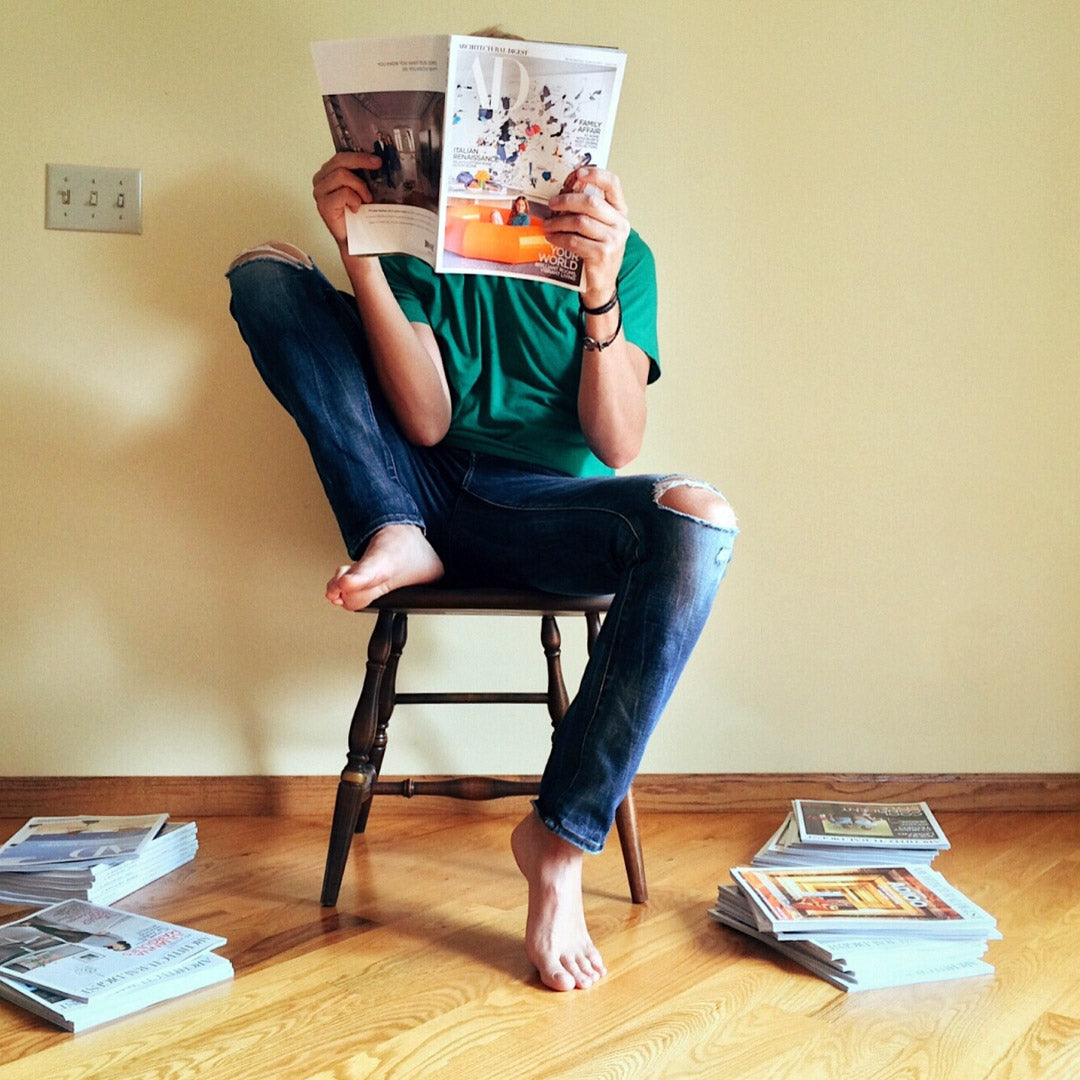 Barefoot man sits in a chair and looks at a magazine.