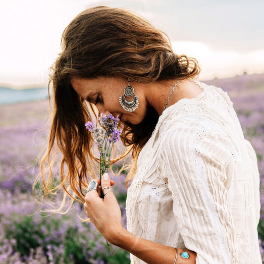 Woman in white stands in a field smelling flowers and de-stressing.