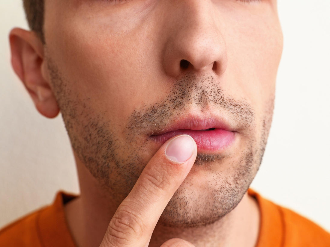 Man touching his lower lip to check for a cold sore, close-up of mouth and stubble