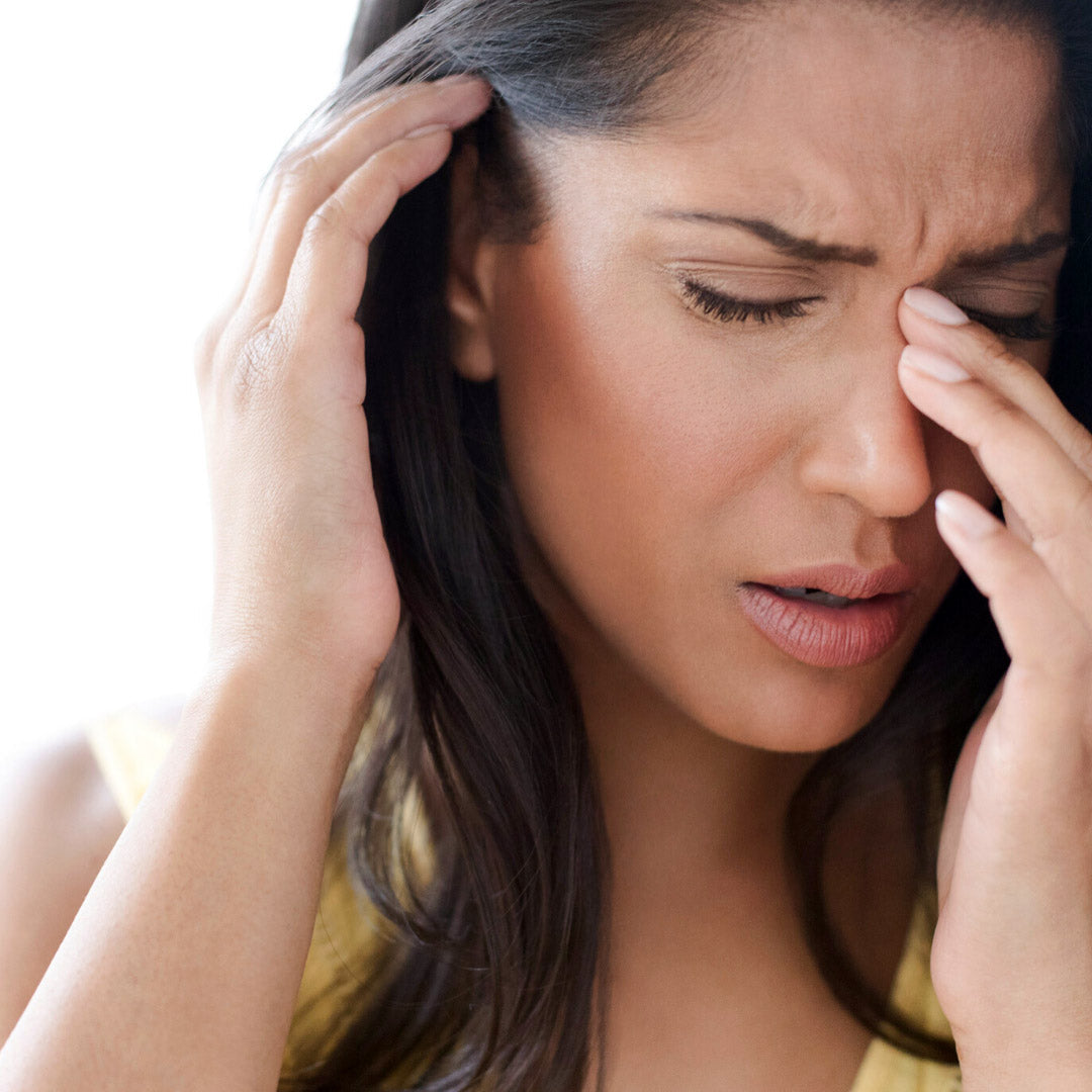 Woman pressing her nose and temple, wincing in pain against a bright background
