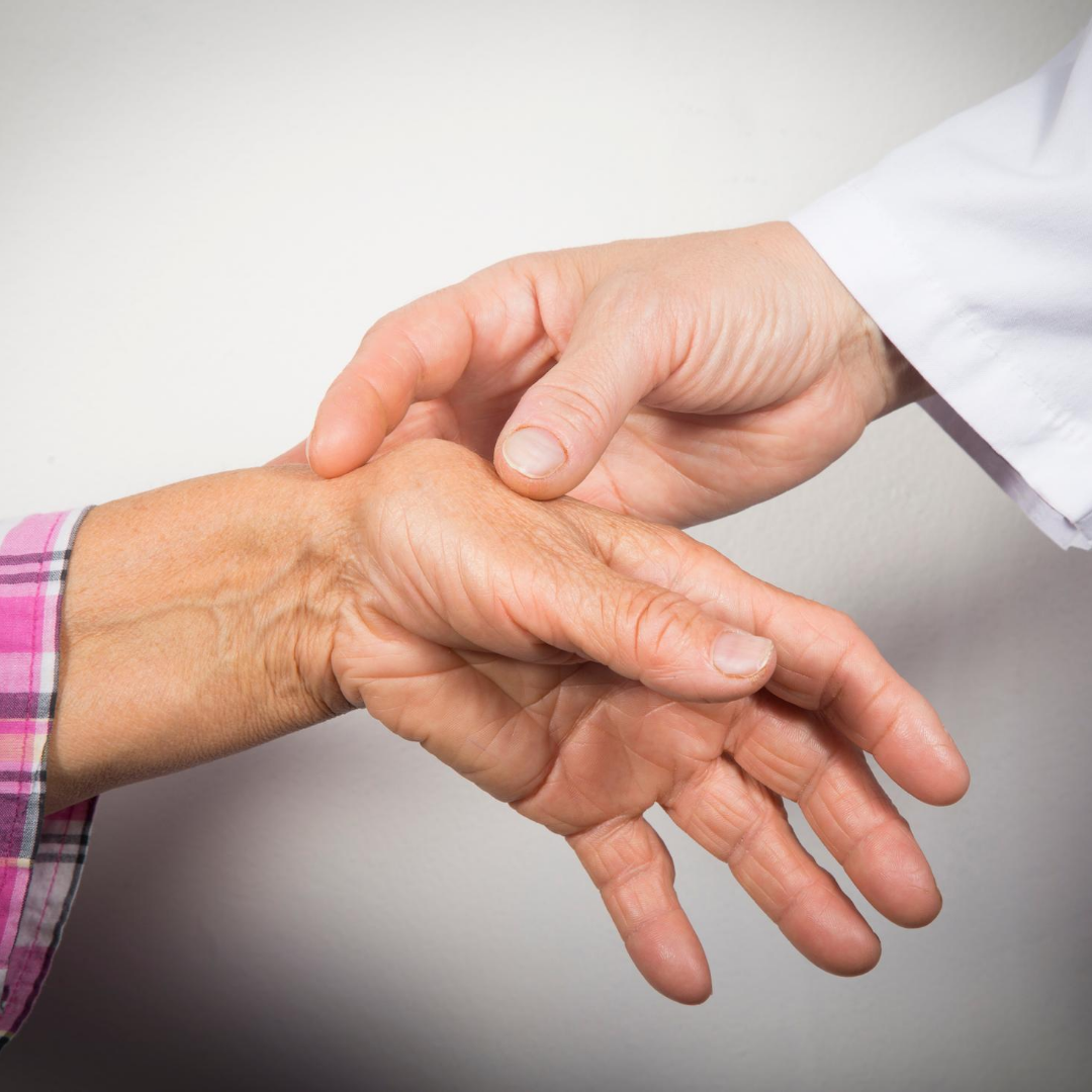 Doctor examining an older patient’s painful wrist and hand against a plain white background
