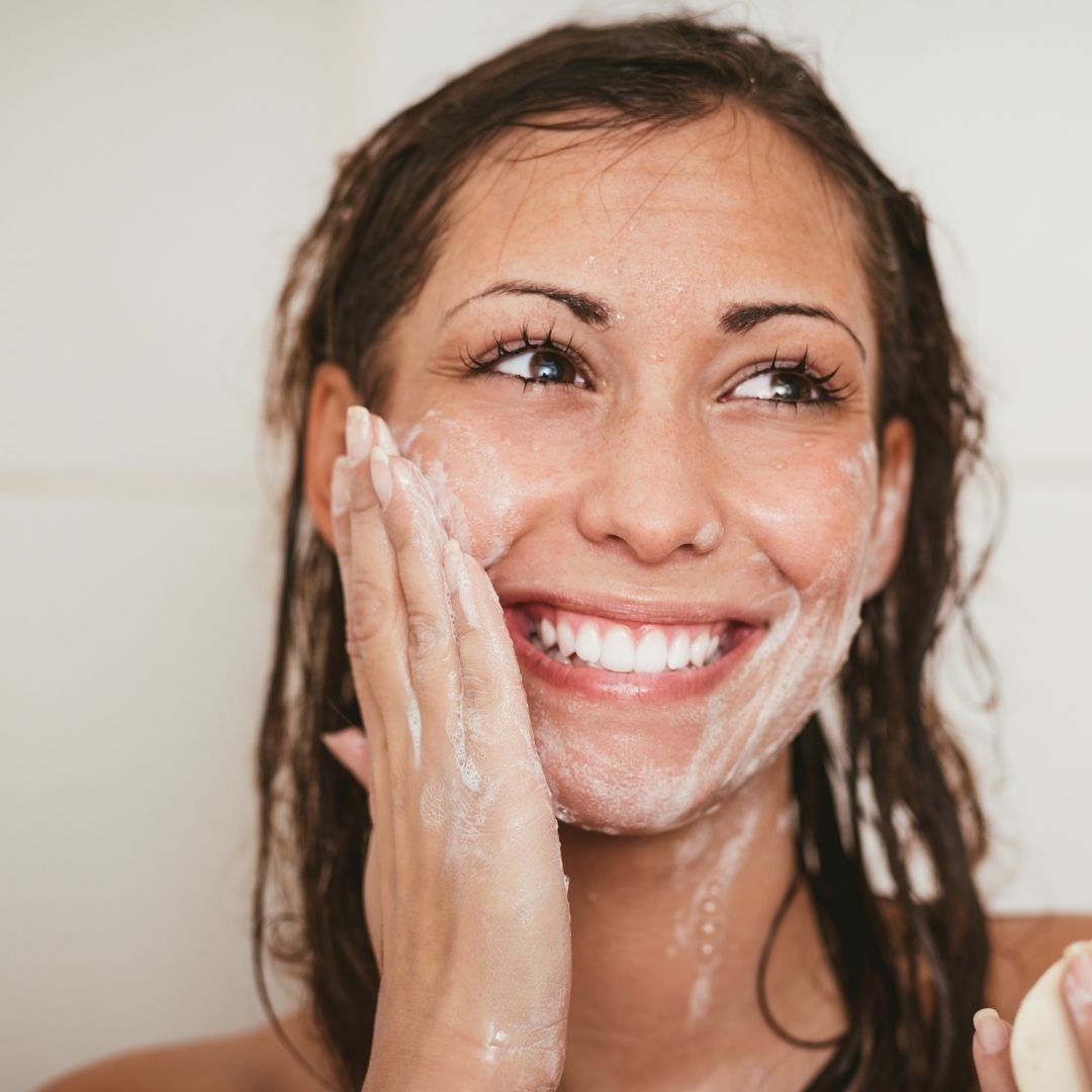 Smiling woman washing her face with a foaming cleanser in a bathroom