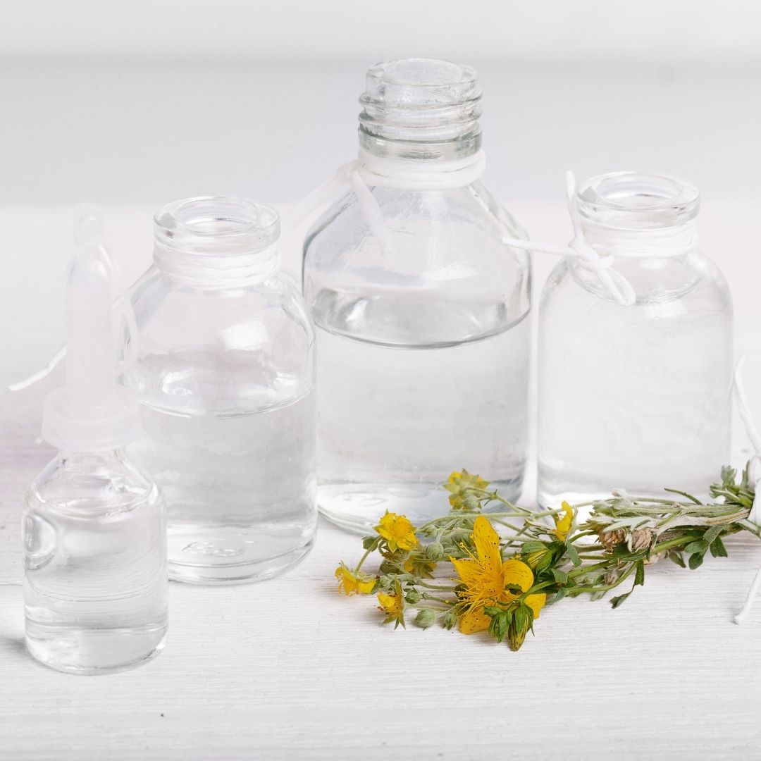 Clear glass homeopathy vials and a dropper bottle with yellow St. John’s Wort flowers on a white surface