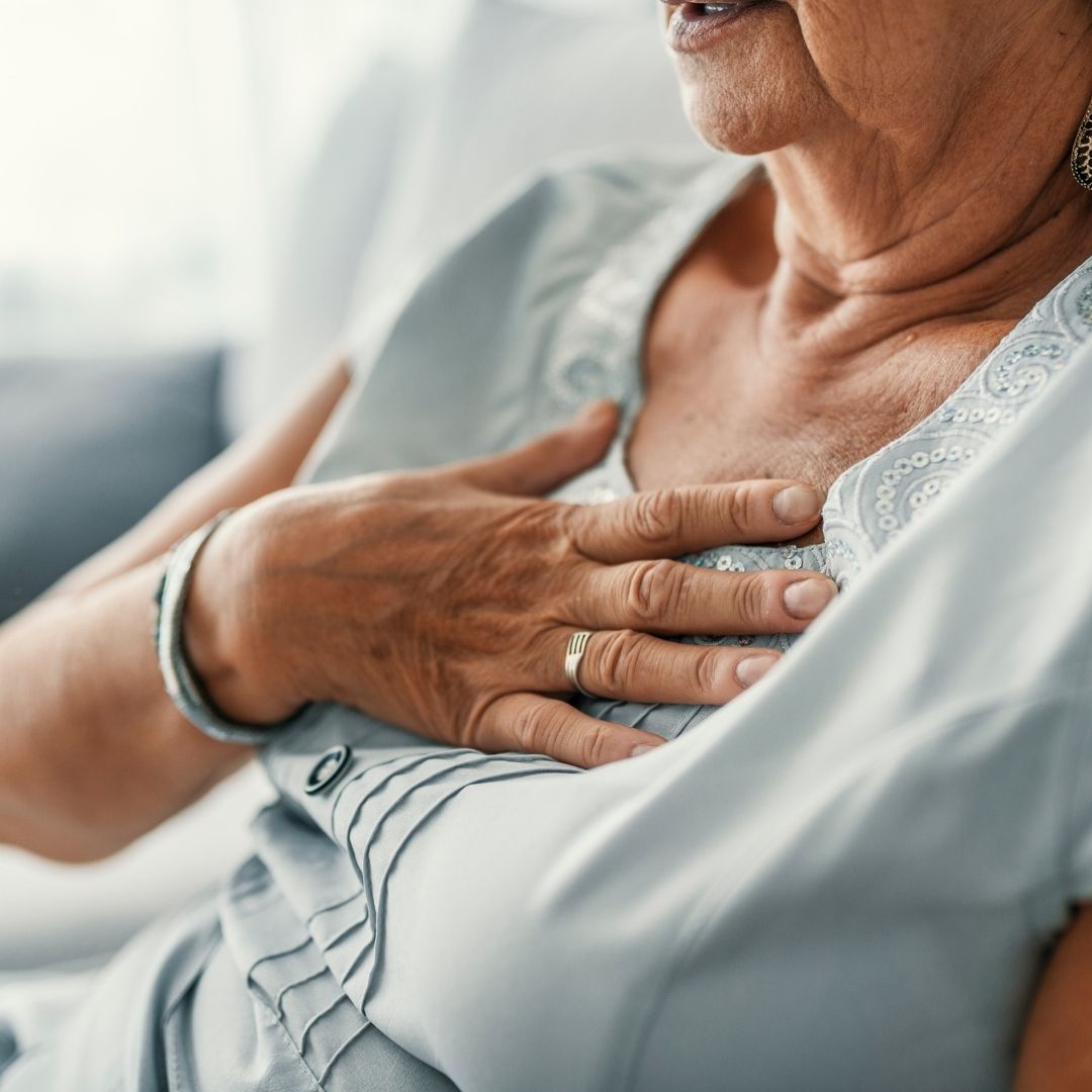 Older woman pressing her hand to her upper chest while seated, appearing to have heartburn or chest discomfort