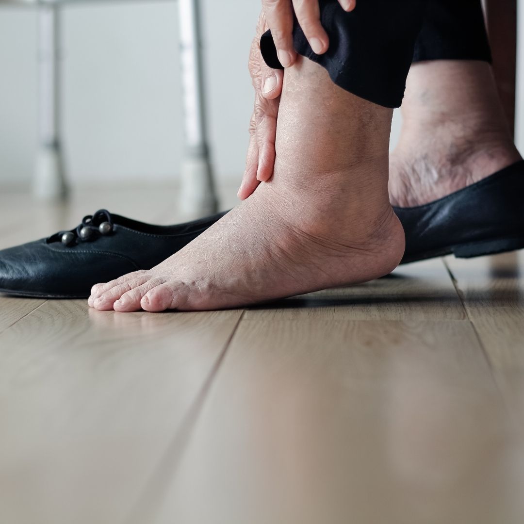 Person holding ankle beside a removed black shoe on a hardwood floor
