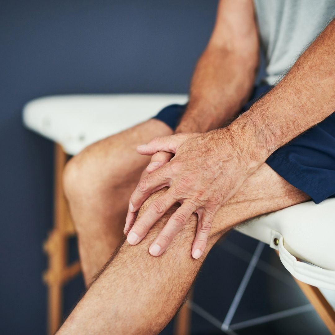 Older man sitting on a medical exam table holding his knee in pain