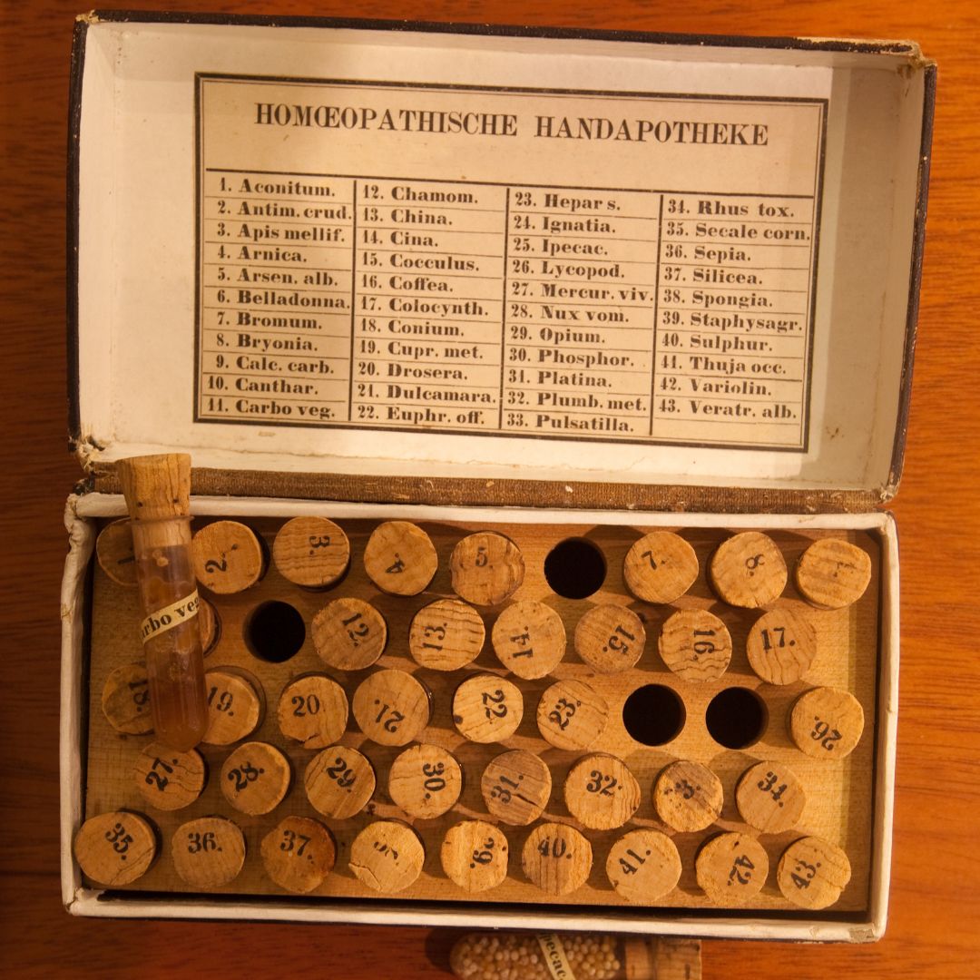 Top-down view of a vintage homeopathic kit showing numbered wooden vials and a printed remedy list in an open box on a wooden surface