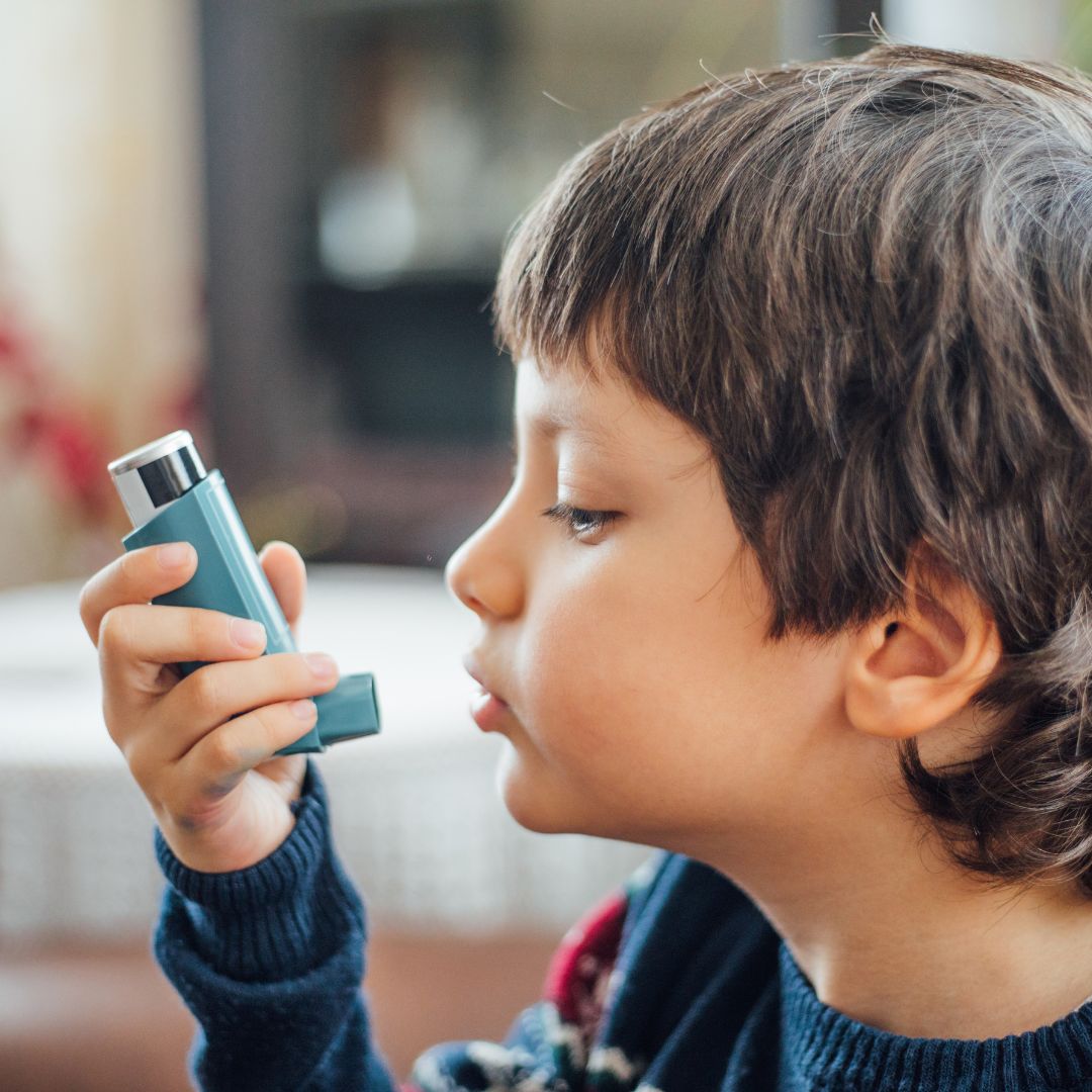 Side profile of a child using a blue inhaler in a living room setting