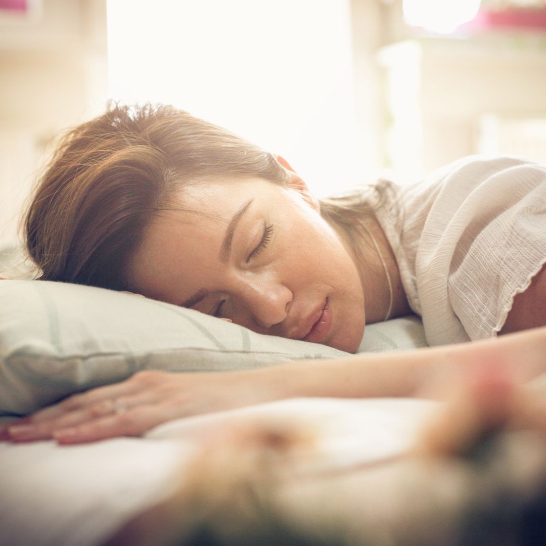 Woman sleeping on her side on a pillow in a sunlit bedroom