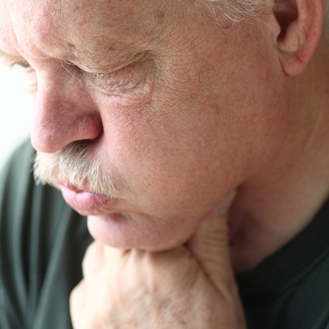 Close-up of older man clutching his throat and wincing, appearing to have throat or chest discomfort