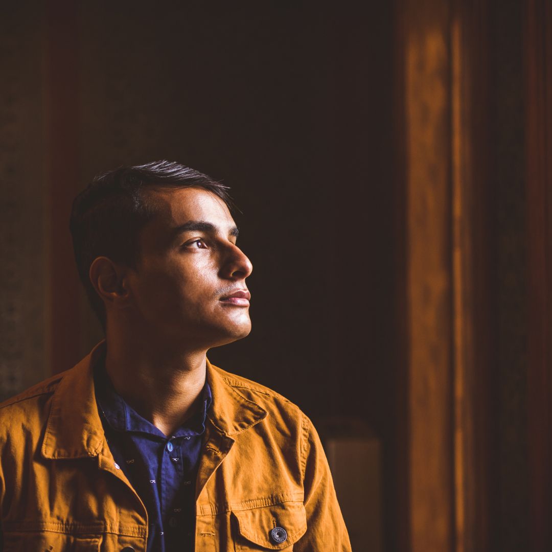 Young man gazing out a window in a dimly lit room, contemplative mood