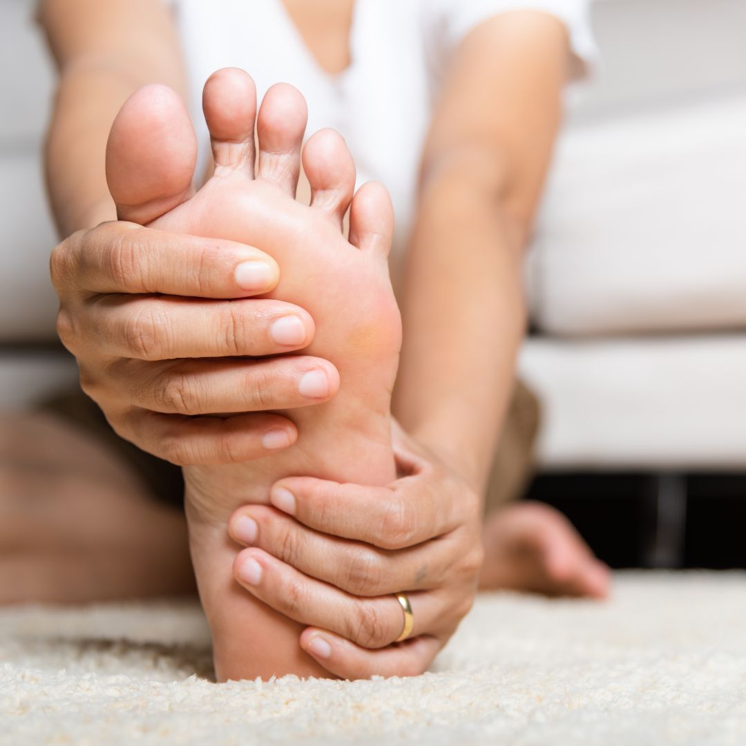Seated person massaging their bare foot with both hands to relieve neuropathy-related foot pain