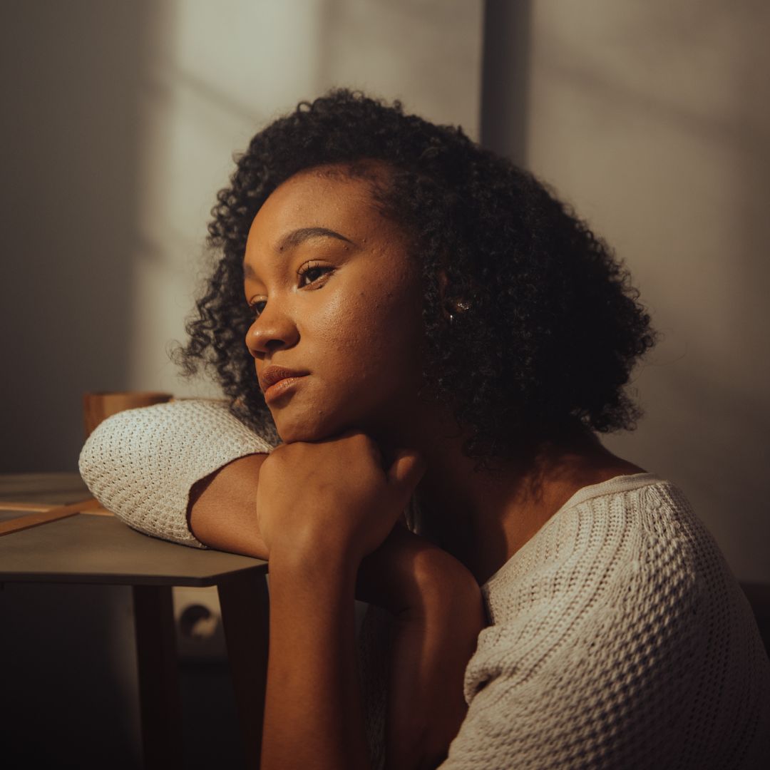 Young woman resting her arms on a table, gazing thoughtfully in warm indoor light