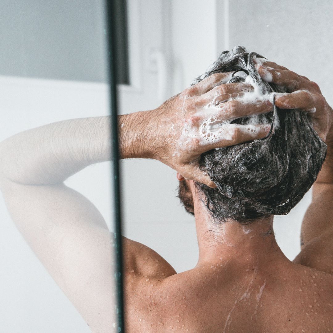Man washing his hair in the shower, back view with soapy lather and water droplets