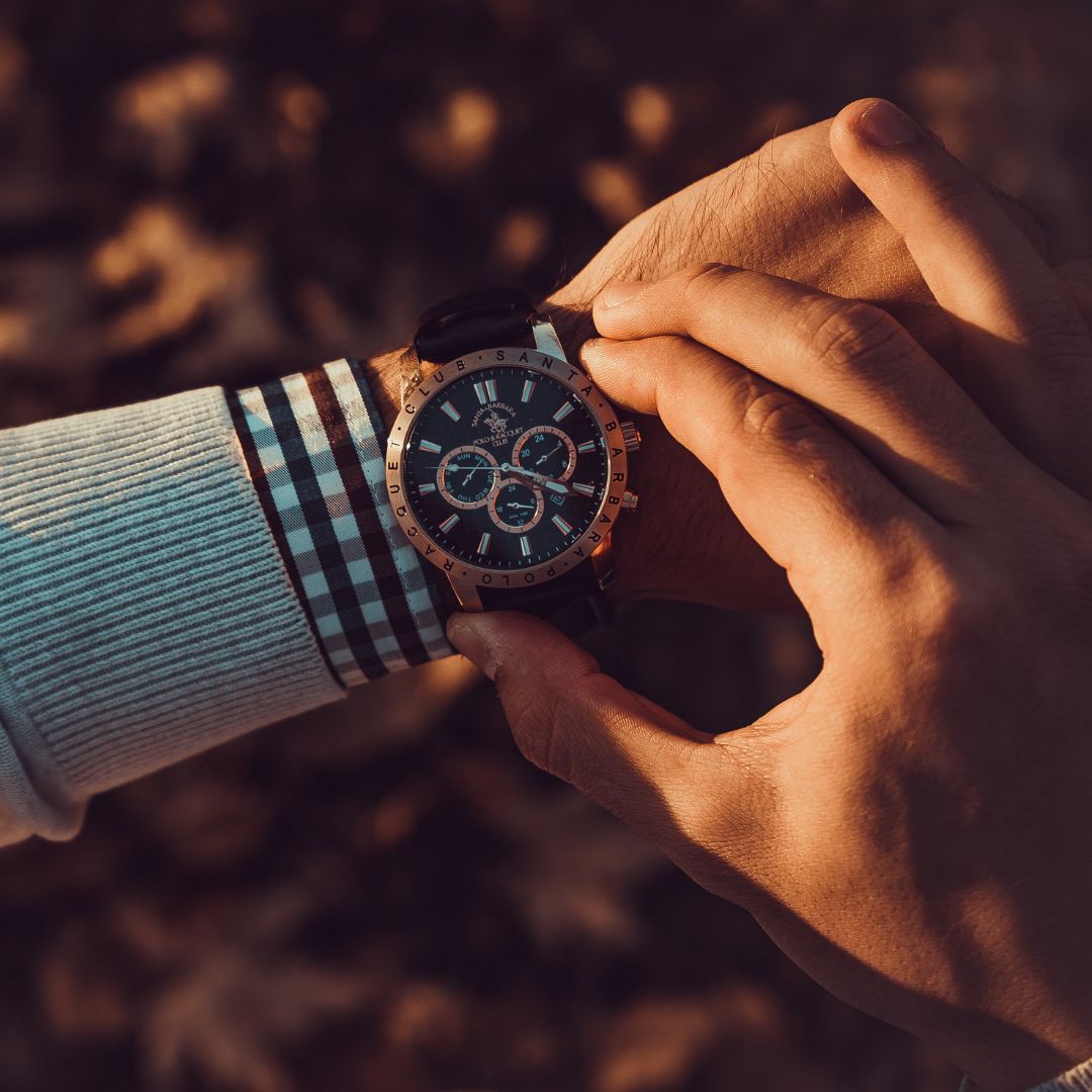Person adjusting a wristwatch over a plaid shirt cuff in warm outdoor light