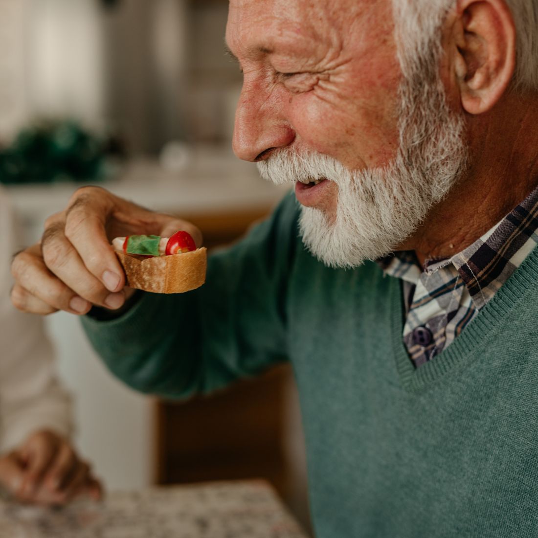 Older man smiling while holding a small appetizer at a holiday table