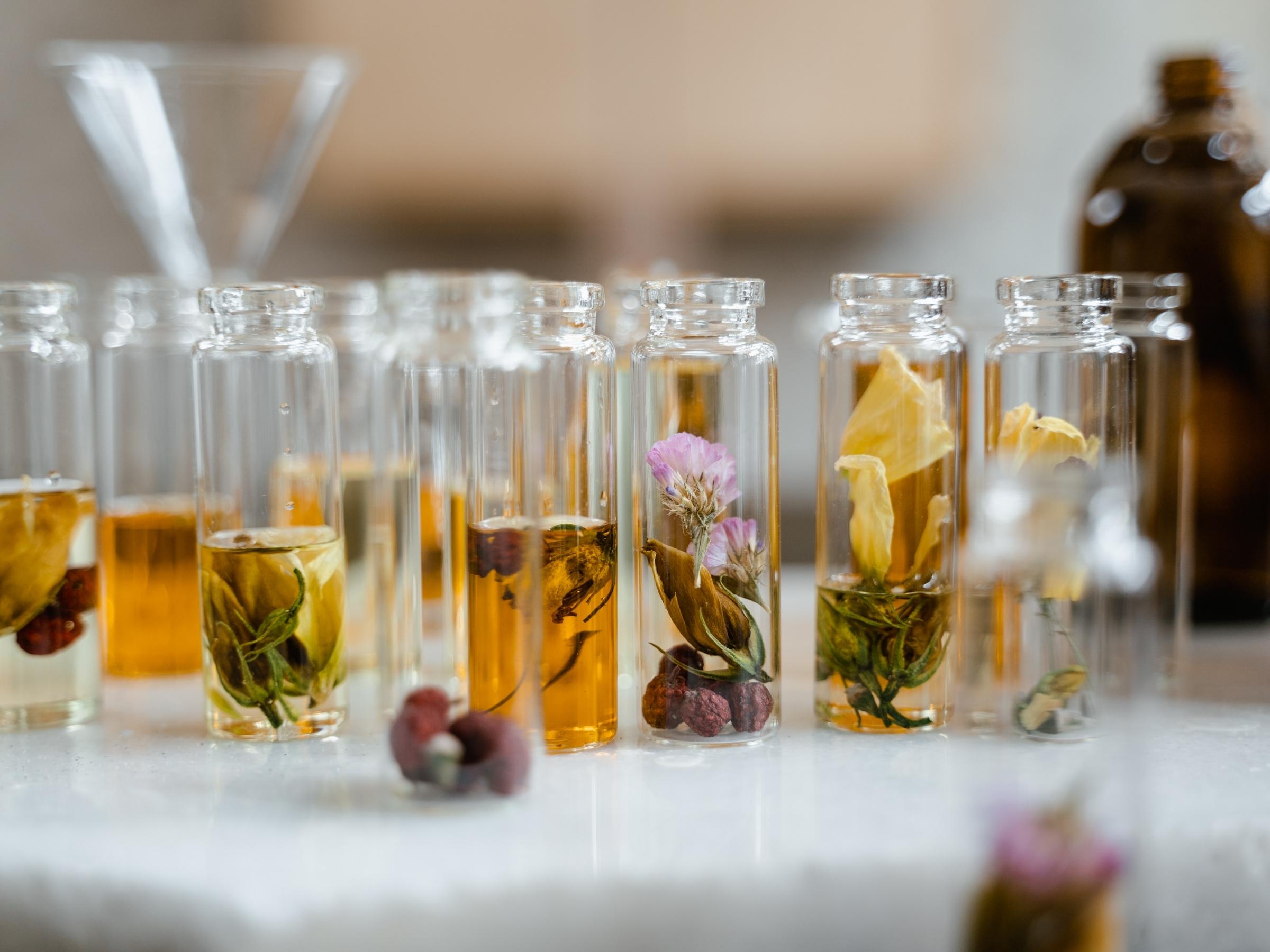 Rows of glass vials holding botanical flowers and golden oils on a marble surface, suggesting natural skincare ingredients
