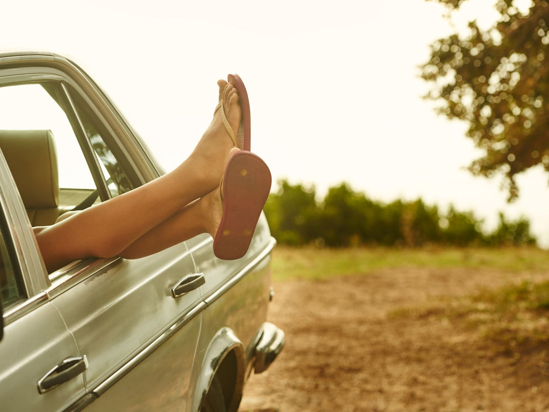 Person’s legs in flip-flops sticking out of a car window on a sunny roadside