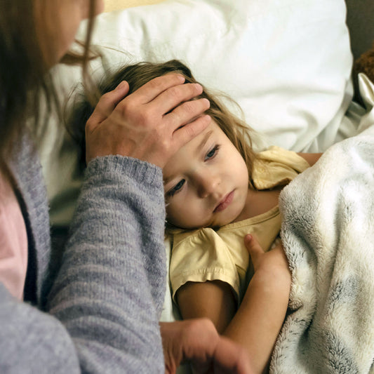 Young child lying in bed under a blanket with a parent checking their forehead for fever, illustrating natural remedies for cold and flu relief.