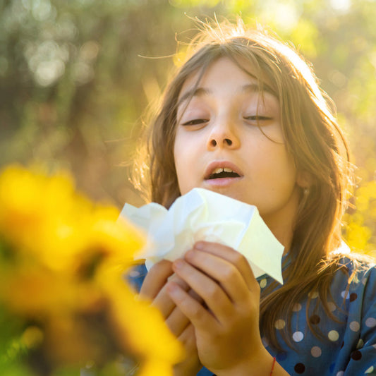 Young girl sneezing from seasonal allergies near blooming flowers.