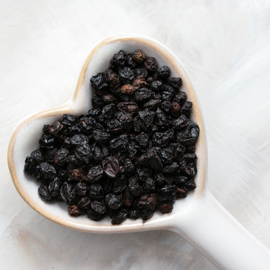 Heart-shaped ceramic dish filled with dried elderberries, known for their immune-boosting properties and natural antiviral benefits