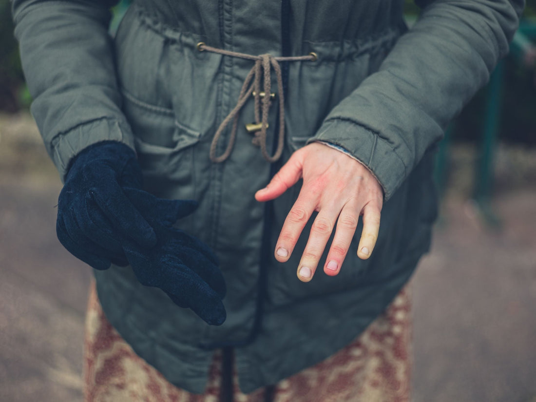 Person removing a black glove to reveal red and pale fingertips while wearing a green winter coat outdoors