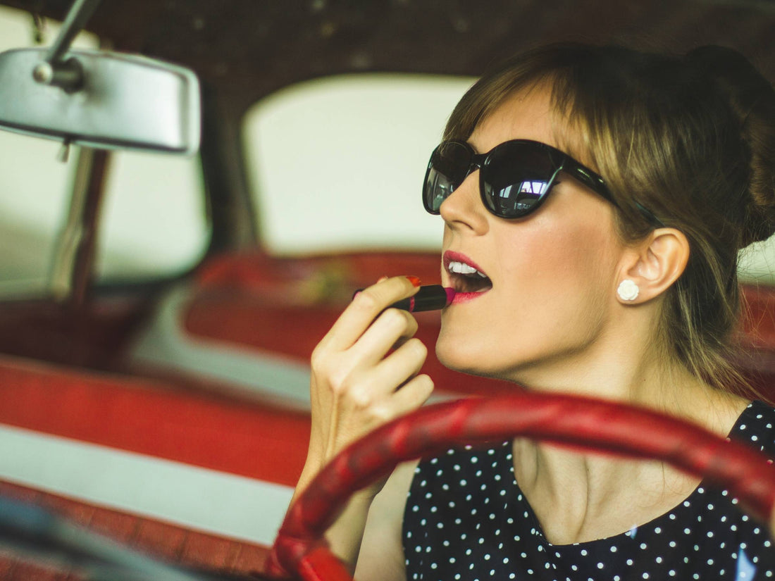 woman applying red lipstick in a rearview mirror in her car
