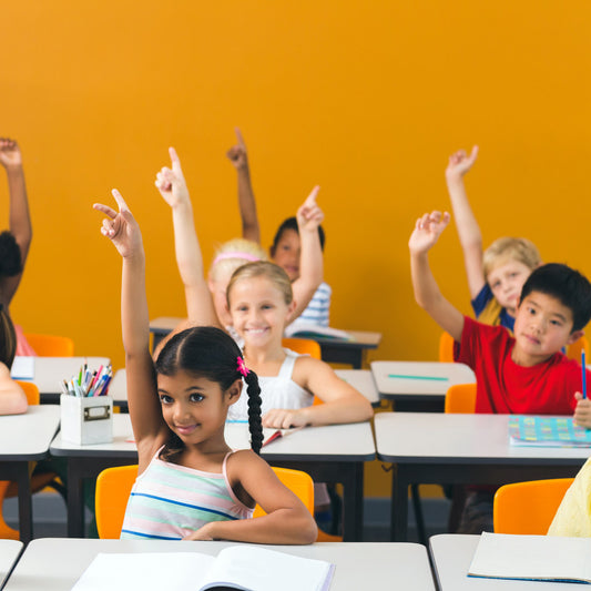 A group of children in class raise their hands while smiling.
