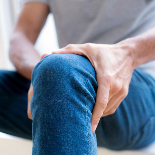 Man sitting in jeans holds knee while dealing with joint pain.