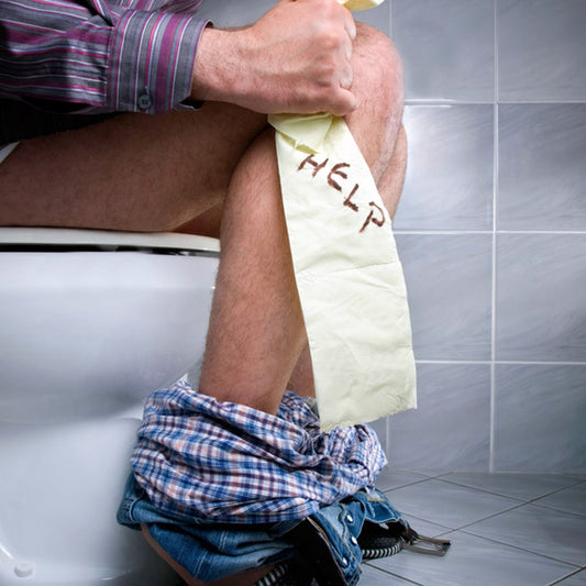Man sits on toilet holding toilet paper with "help" written on it while dealing with external hemorrhoids.