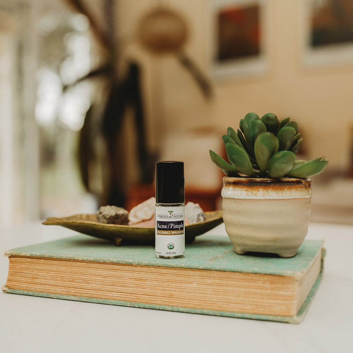 orces of Nature Acne Pimple Rollerball Applicator 4ml bottle on book beside potted plant.