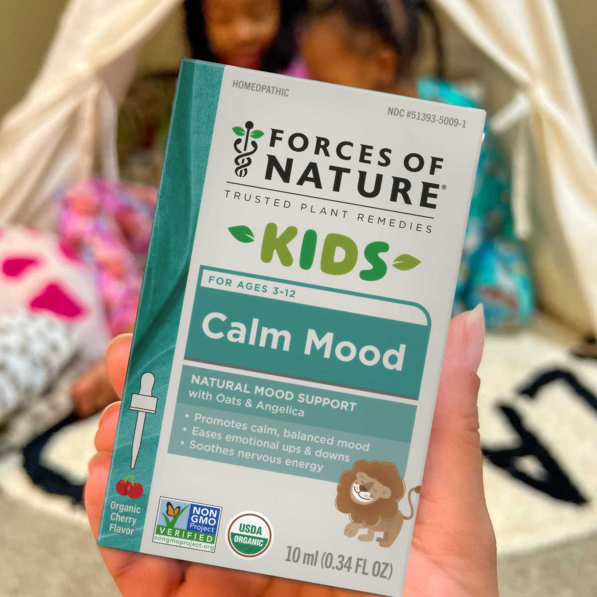 Forces of Nature Kids Calm Mood supplement packaging held by a hand with girls in pajamas in the background.