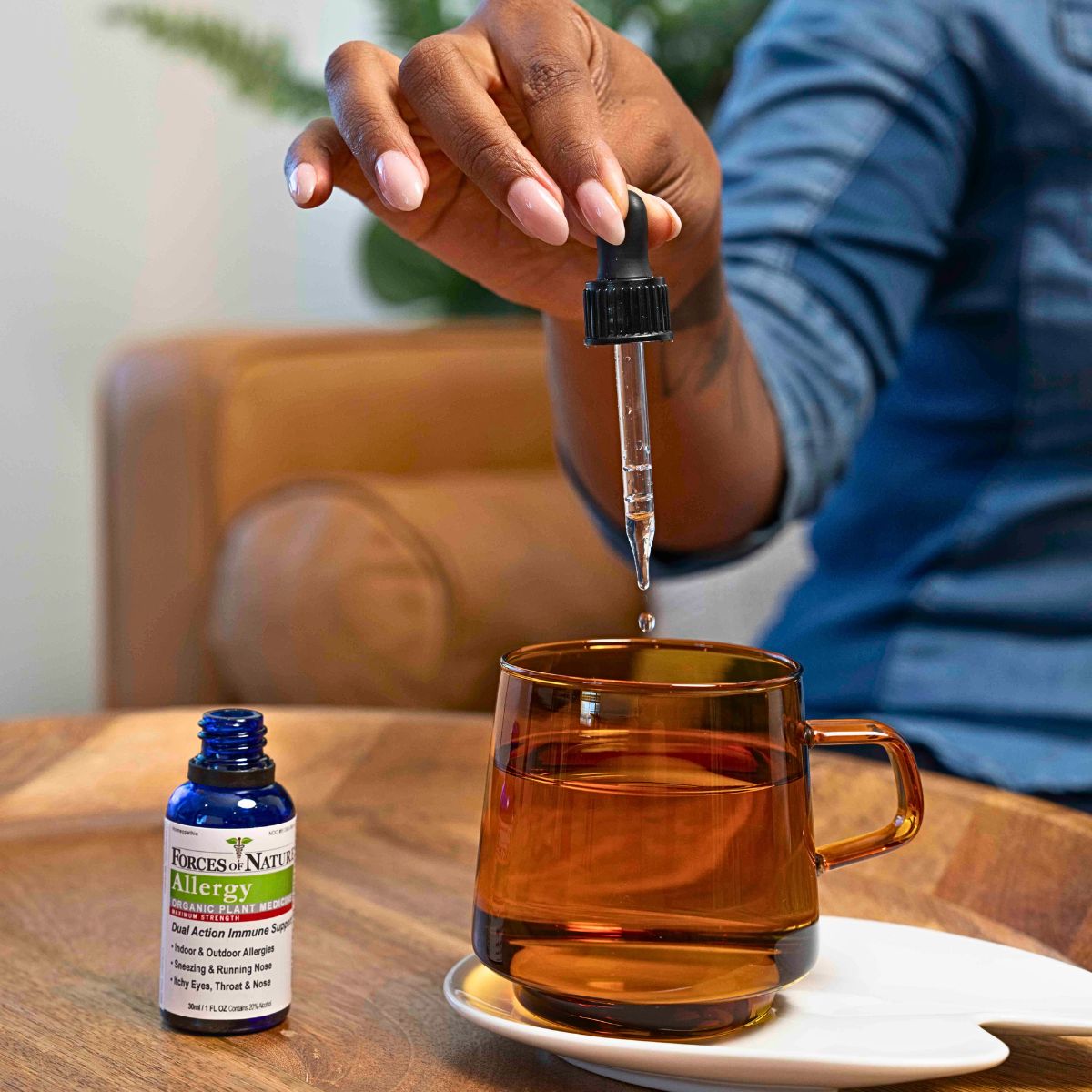 Forces of Nature Allergy Max Strength 30ml bottle on table as hand squeezes drops into mug.